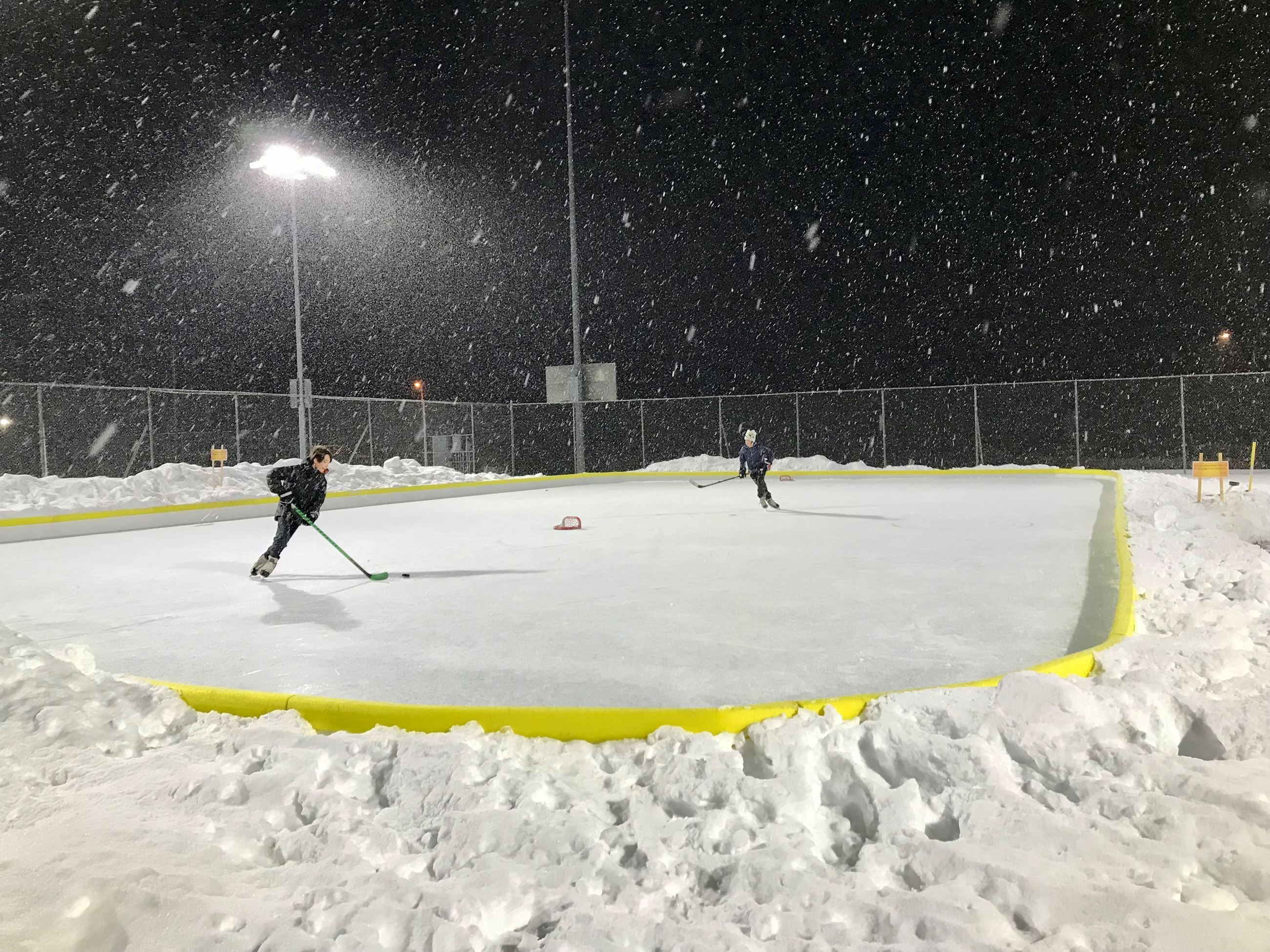 Hockey players skating on the outdoor ice rink in a snow storm. 