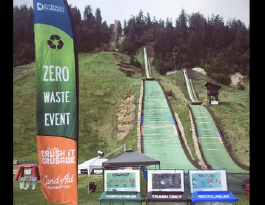 A Zero Waste Event banner and waste station sits on the grass at Howelsen Hill with the ski jumps in